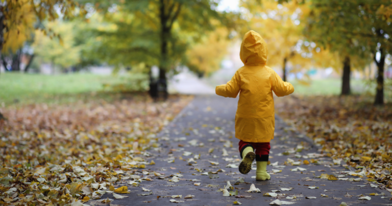 Little kid in a raincoat and boots walking outside