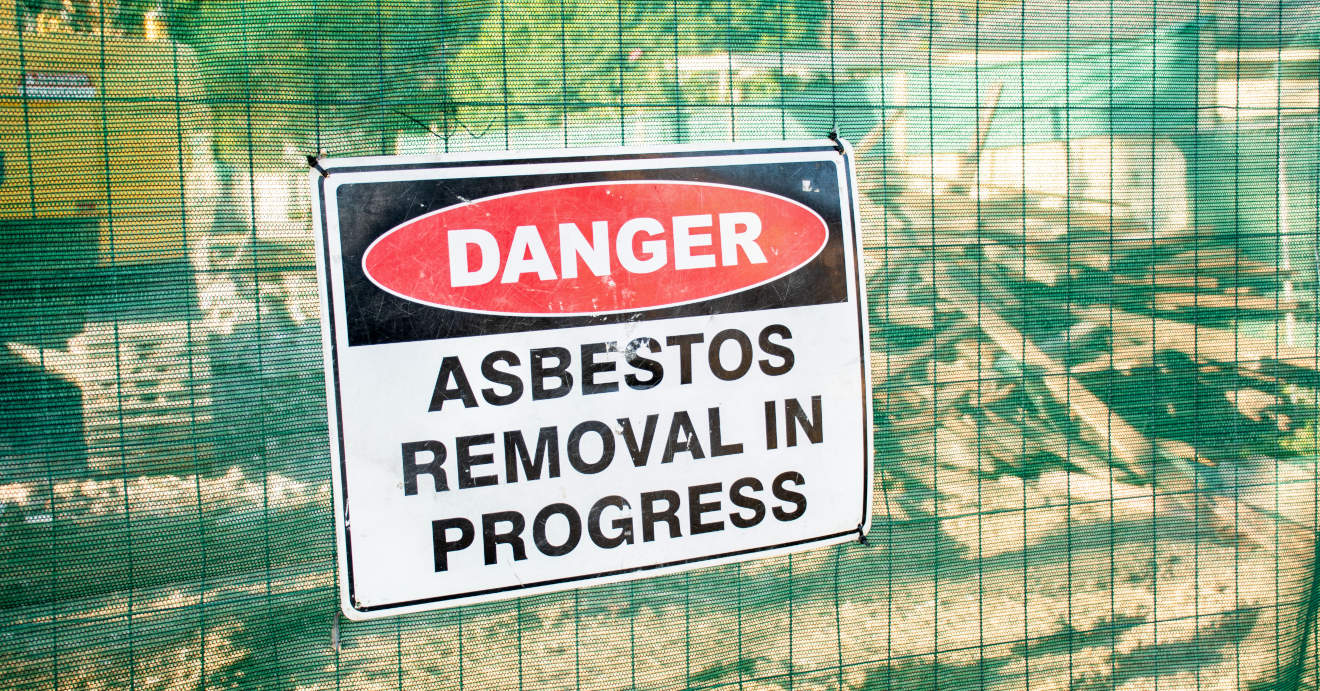 A sign that reads, "Danger: Asbestos Removal in Progress" on a sign outside a construction site