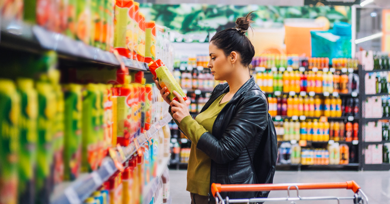 A woman with brown hair looks at the label on a cleaning product in a grocery store