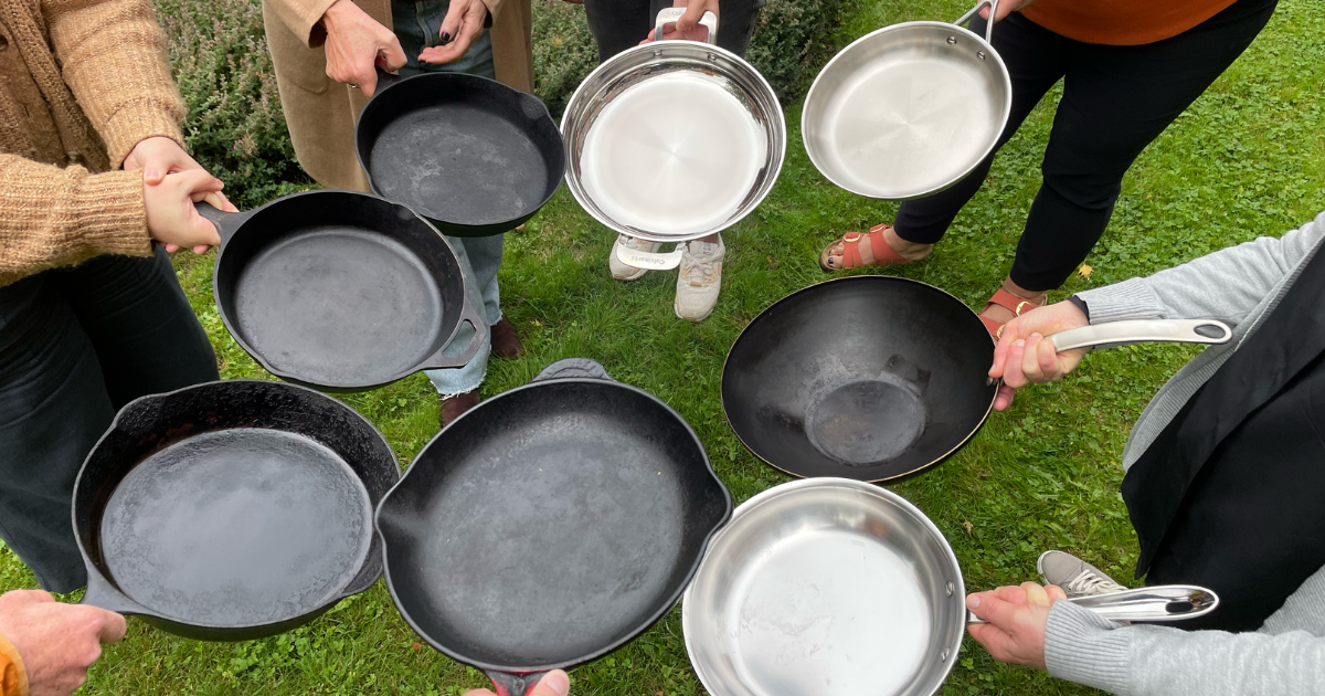 A group of people standing in a circle, holding cast iron and stainless steel pans