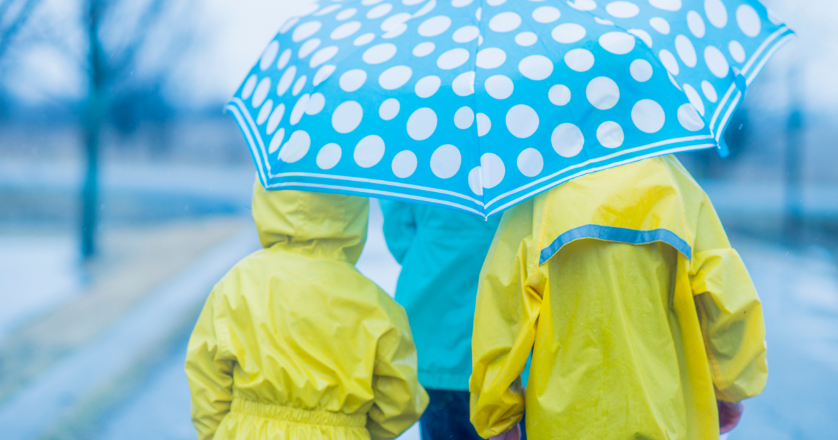 Kids wearing yellow rainjackets made out of vinyl, carrying a blue umbrella.