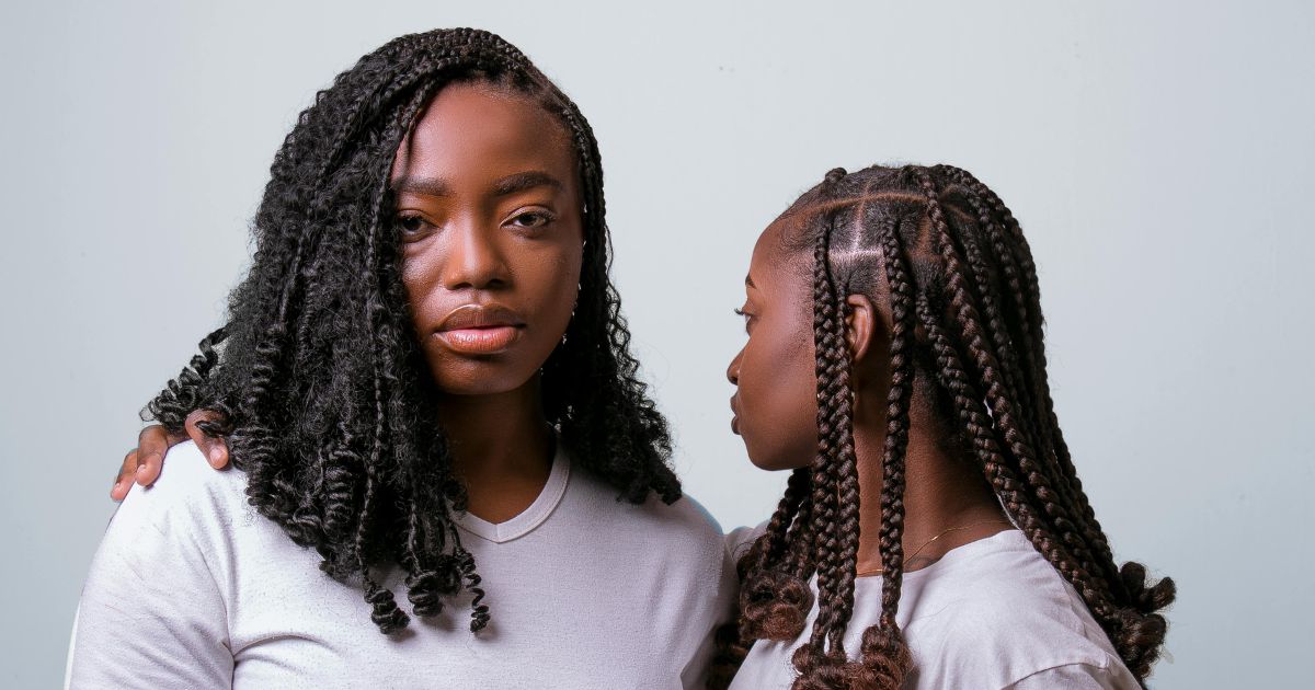 A black woman with long curly hair looking into the camera, next to a young black girl looking at the woman